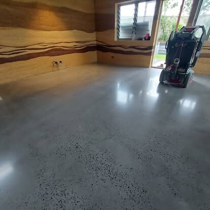 Polished concrete floor mid-project beside a rammed-earth wall with the grinder on site