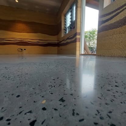 Polished terrazzo-style concrete floor with exposed aggregate beside a rammed-earth feature wall, a real Clark Concrete Polishing job